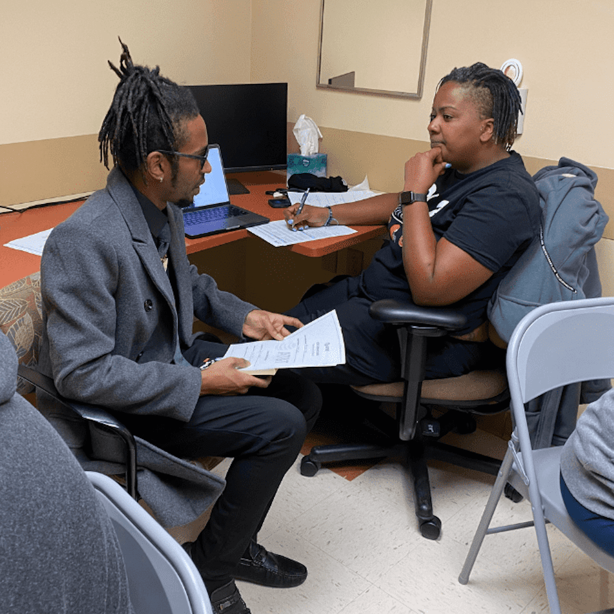 A woman sitting at a computer and a man sitting with her with a piece of paper in his lap