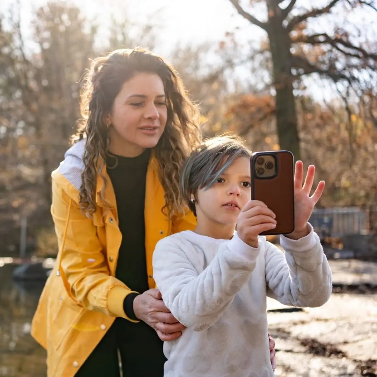 A child taking a photo with his phone and a woman standing behind him