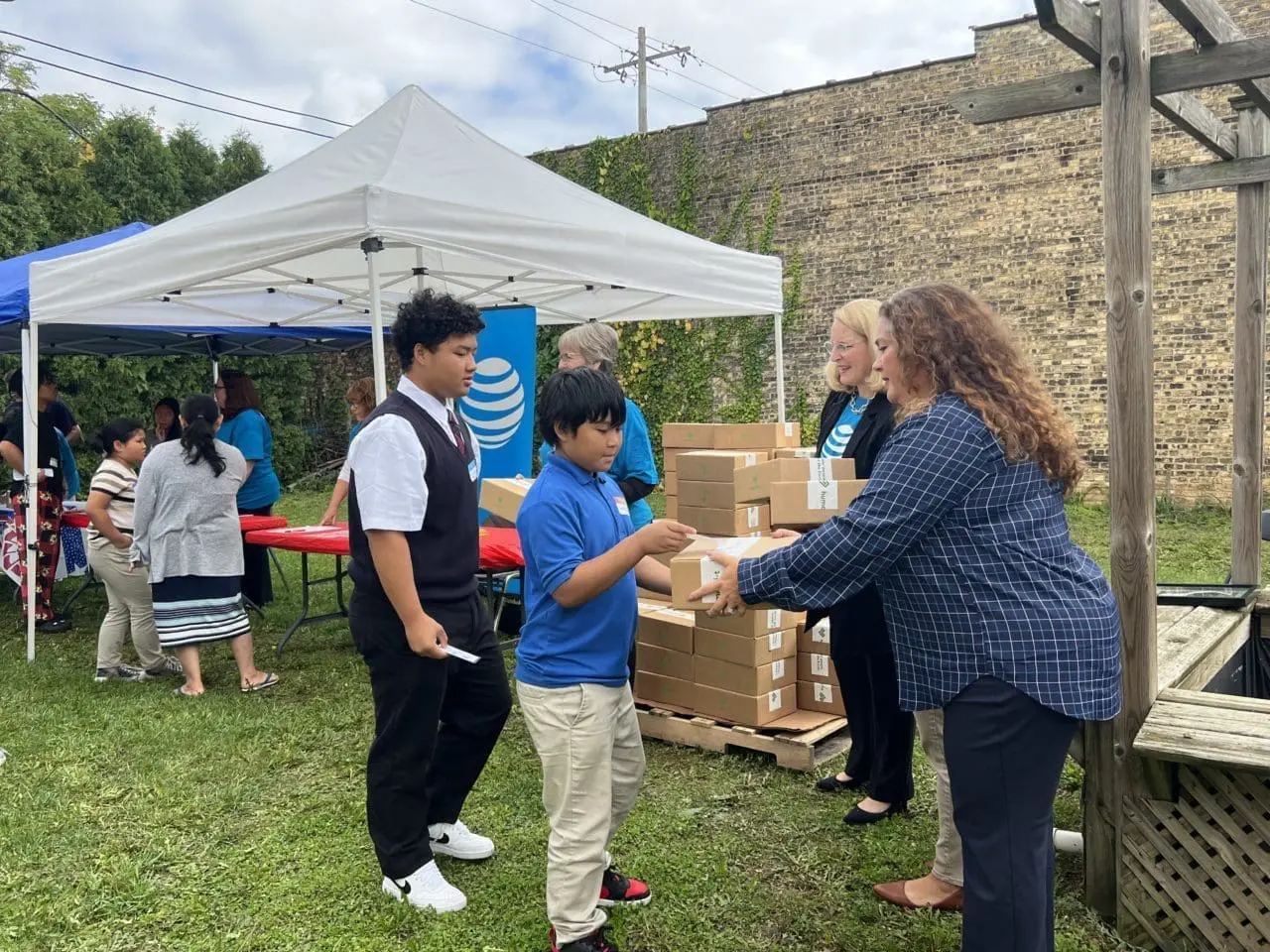 Woman handing a young boy a laptop in a box while outside with a white pop-up tent in the background