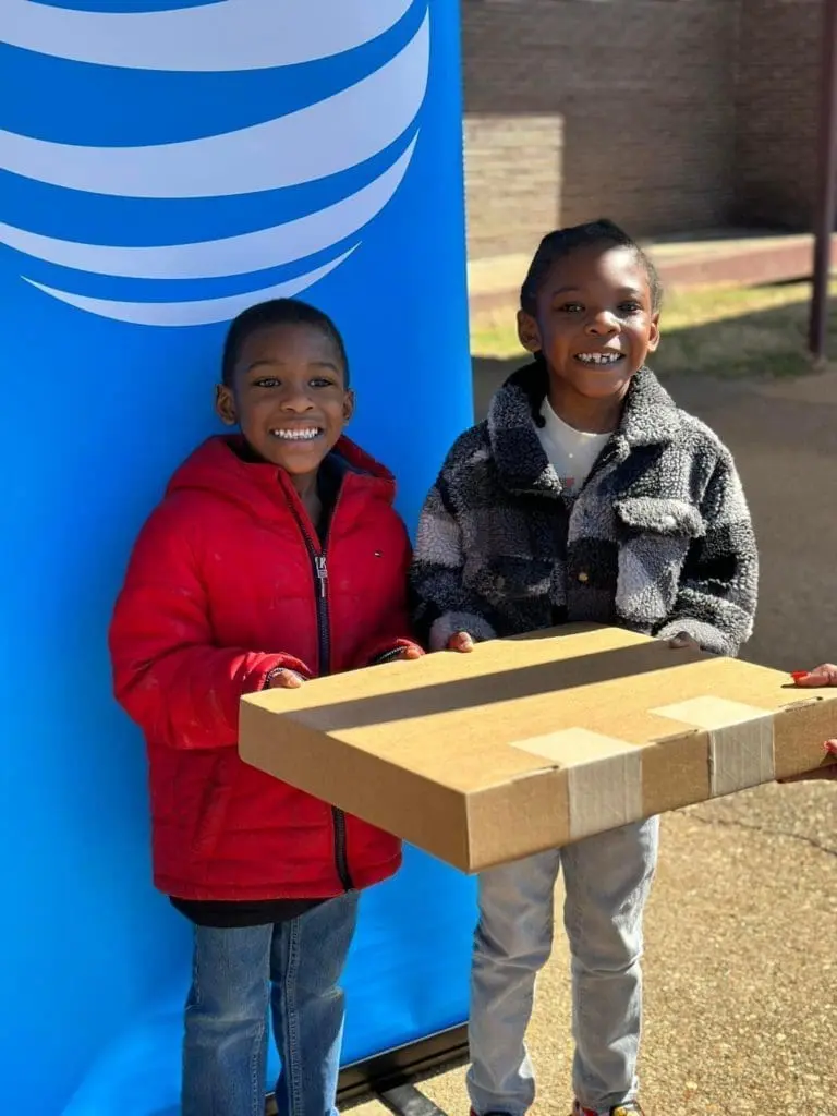 two other young kids smiling holding a box in front of an AT&T banner.