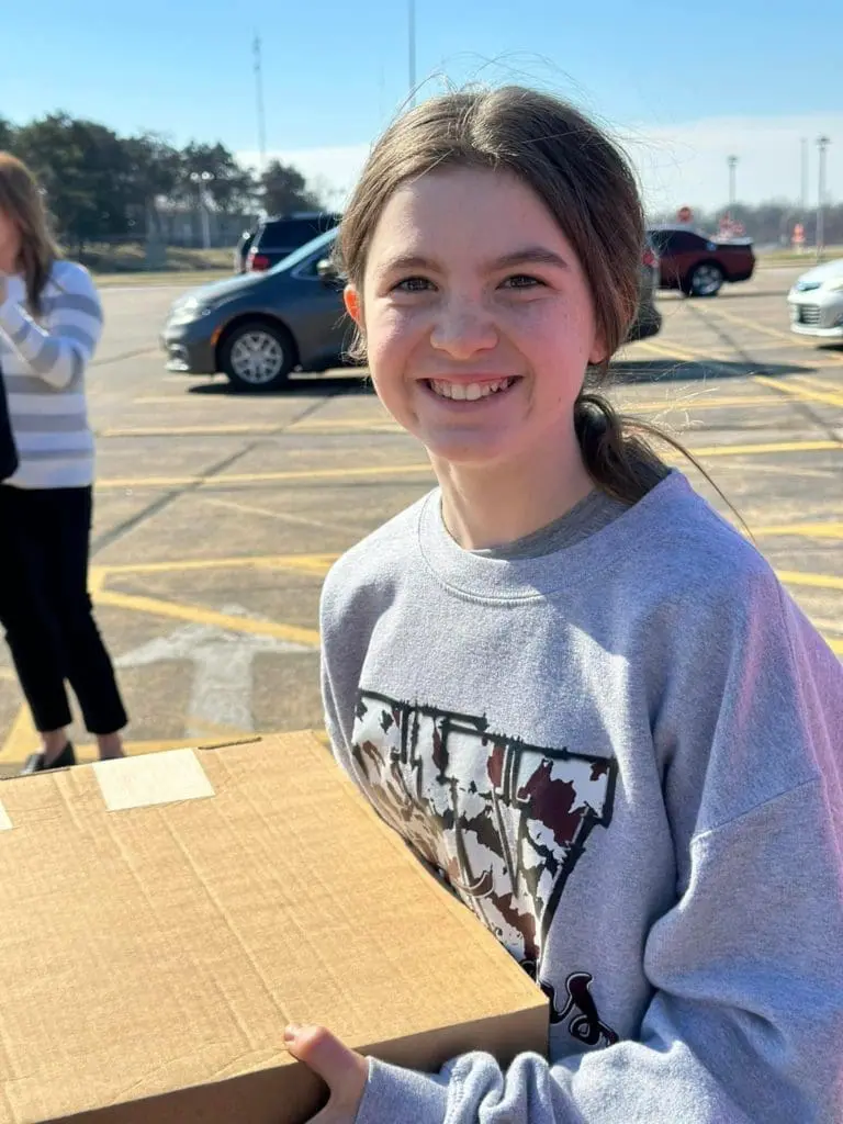A young girl holding a box, smiling.