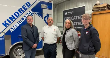 Four people smiling in front of ambulance