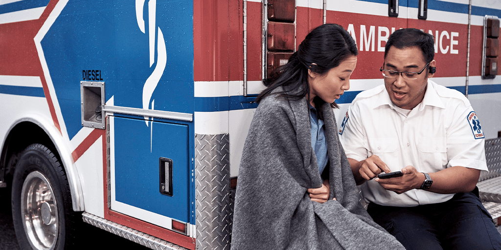 woman wrapped in a blanket talking to a medical professional while sitting at the back of an ambulance