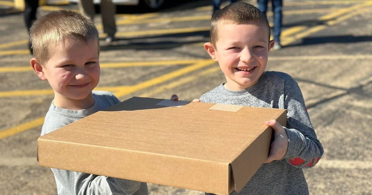 Two young kids smiling and holding a box.