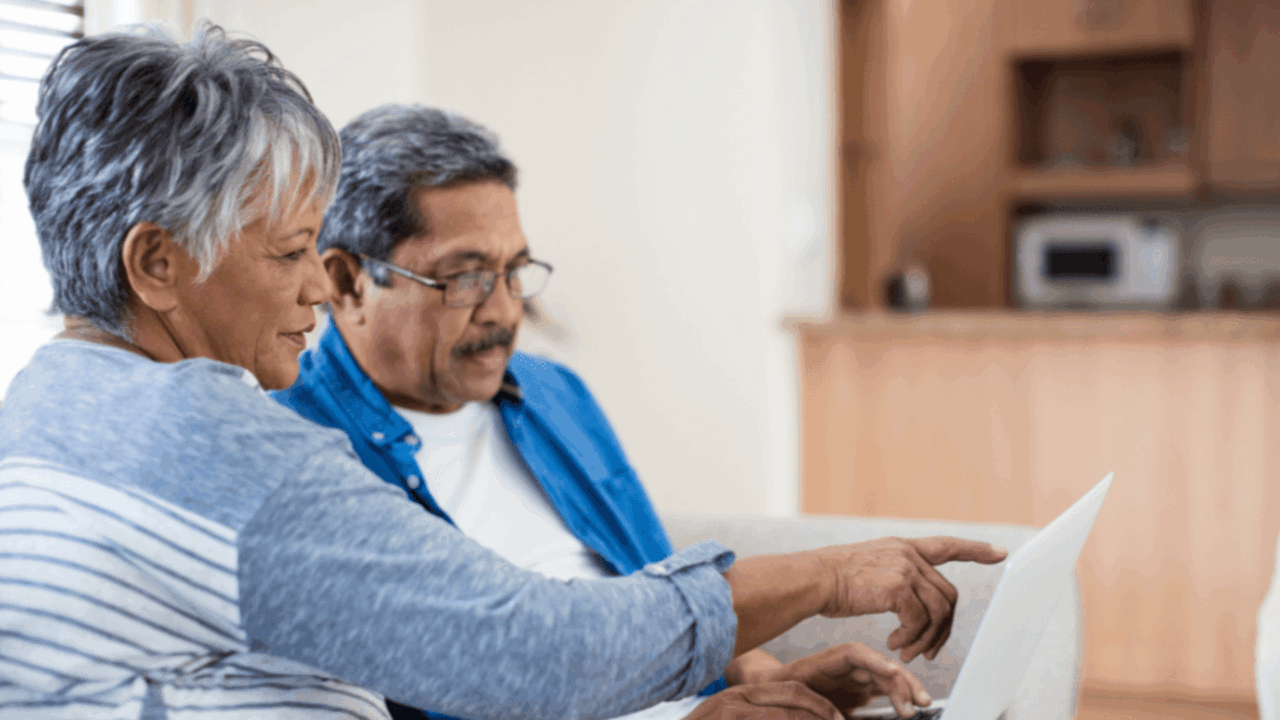 An elderly couple pointing at a laptop.
