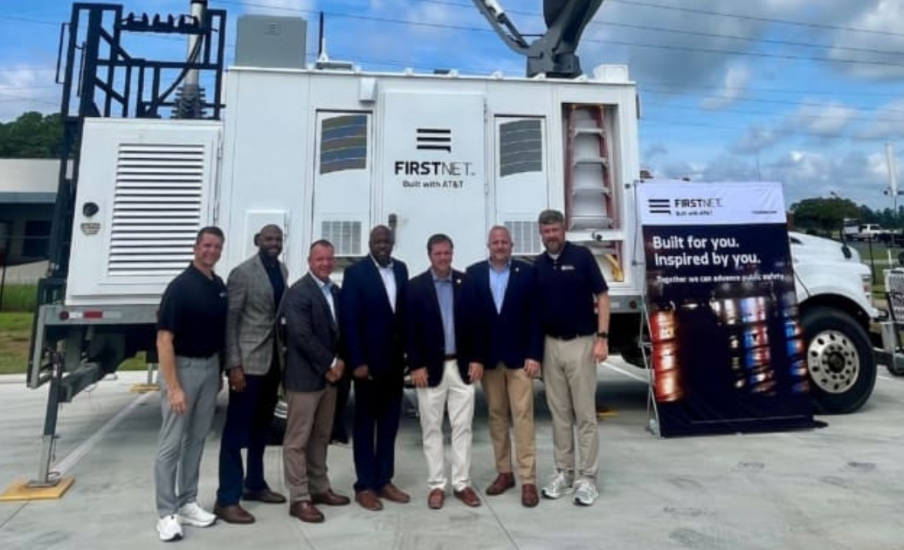 A group of seven people standing in front of the same truck with a satellite dish on top.