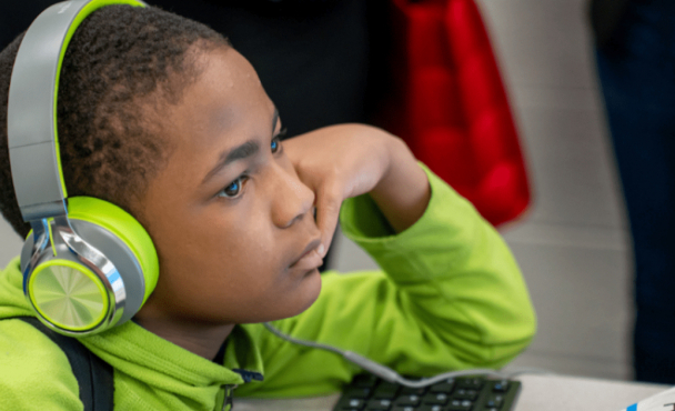 A child with headphones over the ears looking at a computer monitor