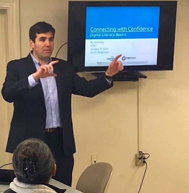A person talking in front of a wall mounted tv