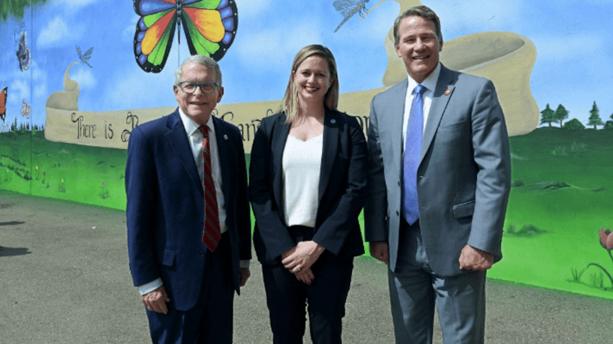 Three people, including the Governor of Ohio, posing for a photo in front of a mural