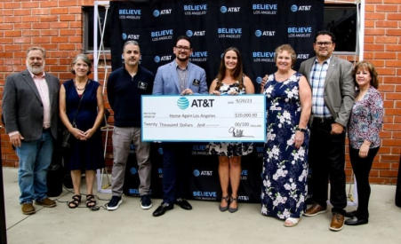 Individuals smiling while posing together against a brick wall behind a check from AT&T in business casual dress