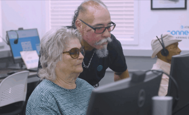 An older man and woman at a desktop computer in a computer lab