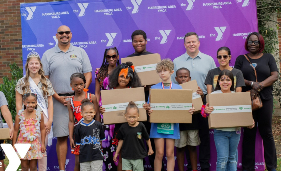 A group of children and adults holding boxes in front of a YMCA banner