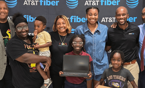 Family holding a laptop in front of an AT&T Fiber banner