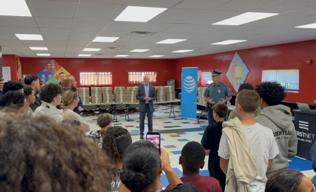 Two people standing at the front of a room speaking to a room full of children