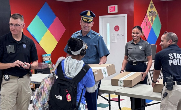 A child walking up to a table talking with a Massachusetts State Trooper