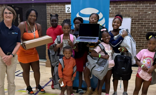 Group of children pose with their laptops and an AT&T volunteer