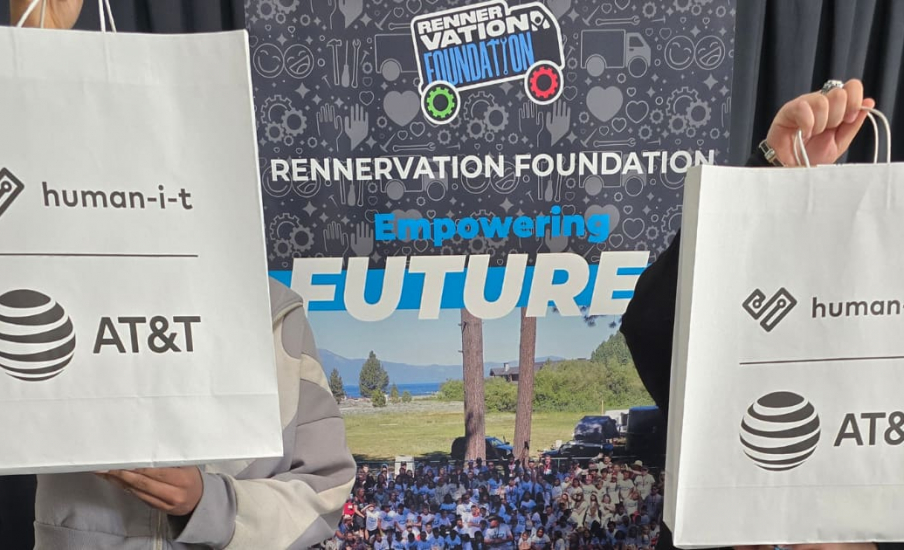 Two recipients holding AT&T and Human-I-T bags in front of an event banner.