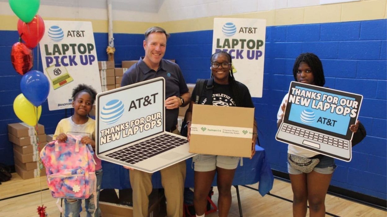 An adult and three kids holding laptop shaped signs and a box
