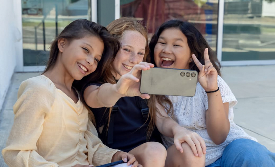 Three tween girls smiling at phone.