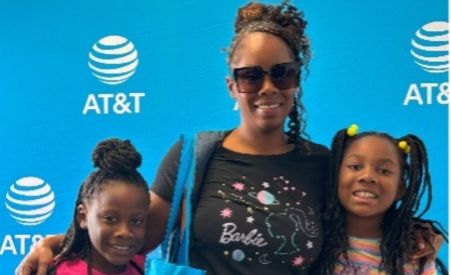 A woman and two kids in front of an AT&T banner smiling