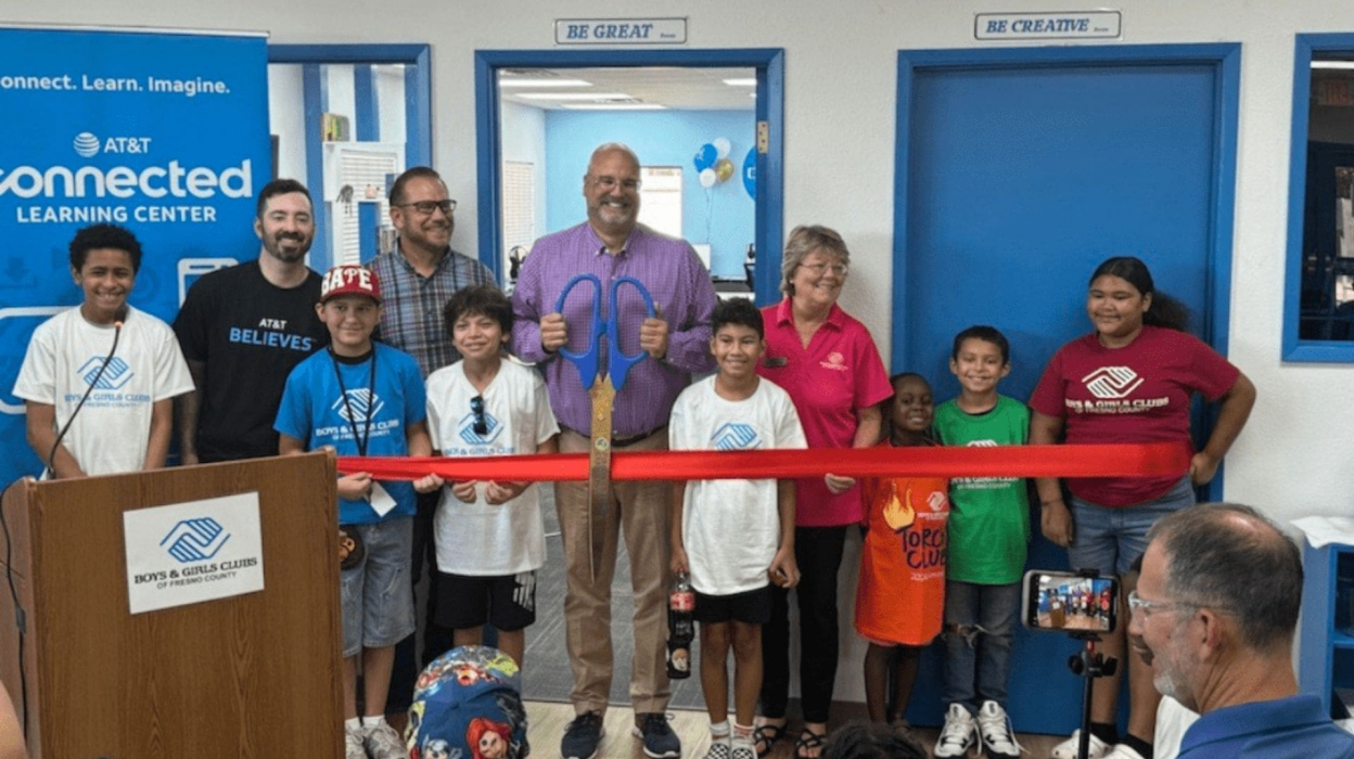 Kids standing in front of a ribbon with an adult about to cut it