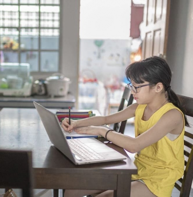 A girl writing and looking at a laptop