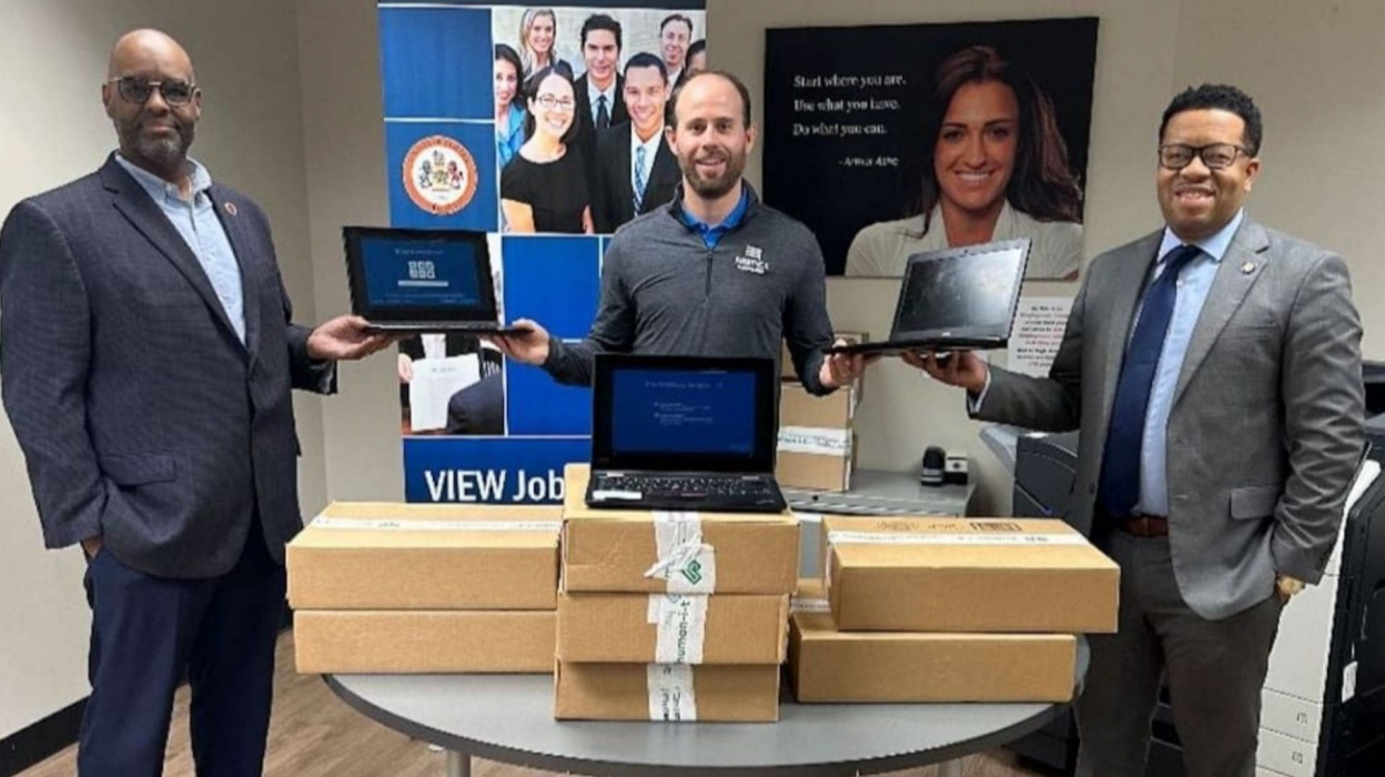 A person in the middle of two people, handing each person a laptop